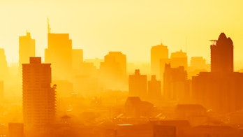 The photo depicts Sunrise over modern office buildings in business district center of Bangkok. Skyline view of cityscape with sunlight and flare in warm light color tone. Construction business concept