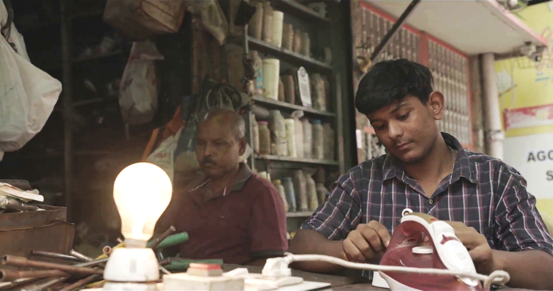 Two men sewing clothes using light from a lightbulb - 3DEN programme