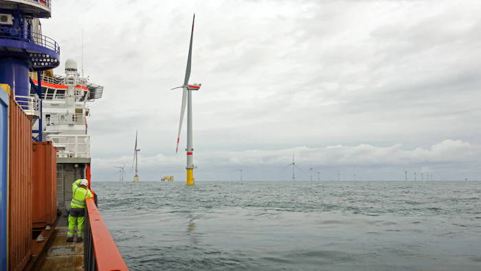 the Photo depicts a Technician standing on transfer vessel deck in the morning and looking on offshore wind farm and offshore platform around