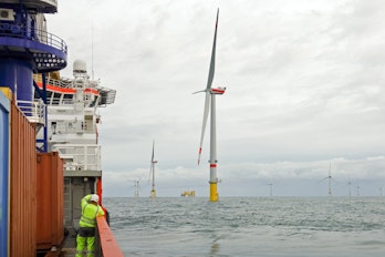 the Photo depicts a Technician standing on transfer vessel deck in the morning and looking on offshore wind farm and offshore platform around