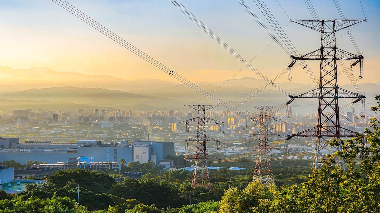 La foto muestra una vista de postes y líneas eléctricas con edificios y montañas al fondo Shutterstock 2325254401
