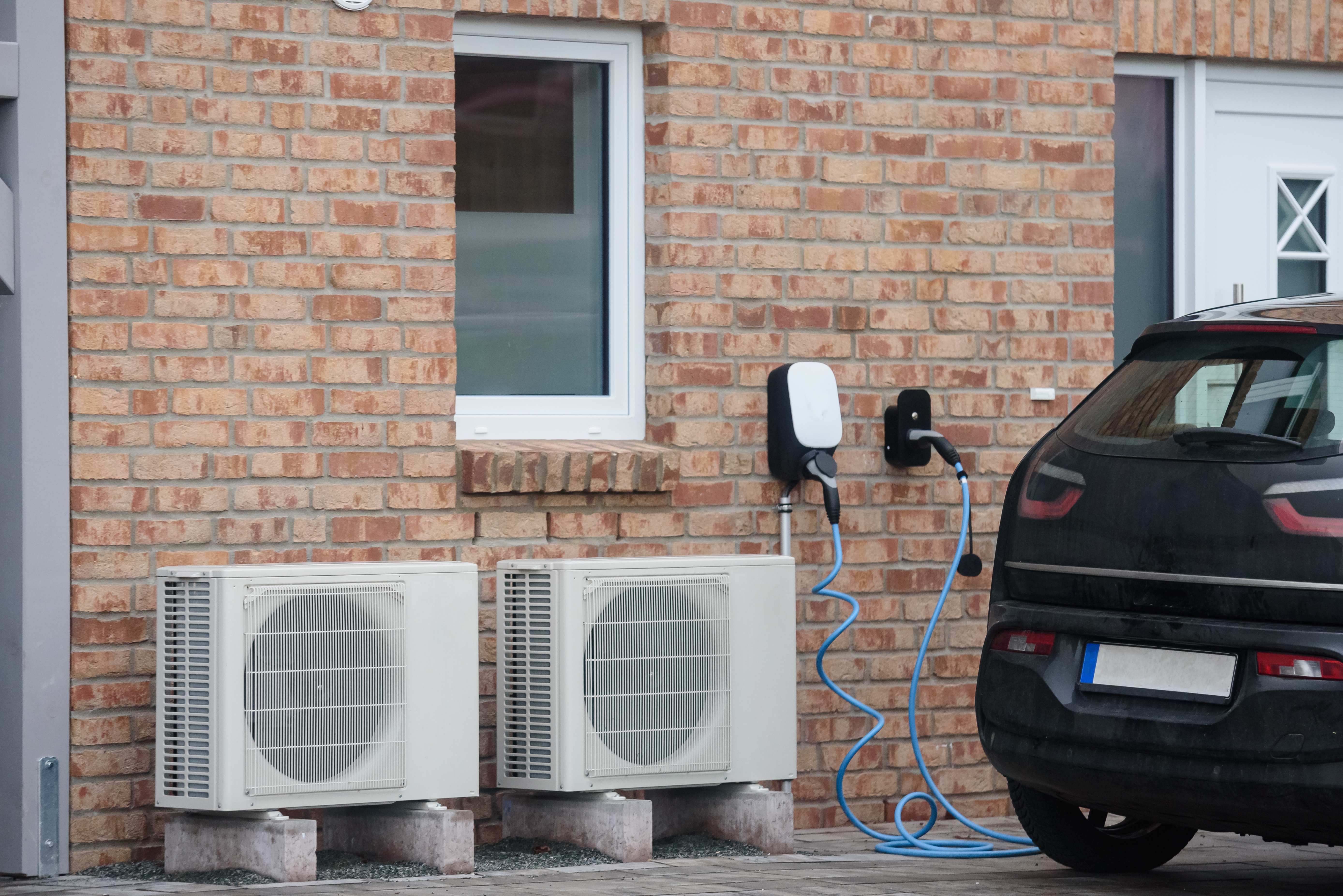 Sustainable living with EV charging and heat pumps. Modern home equipped with energy-saving solutions, including two heat pump units and an electric vehicle (EV) charging station.