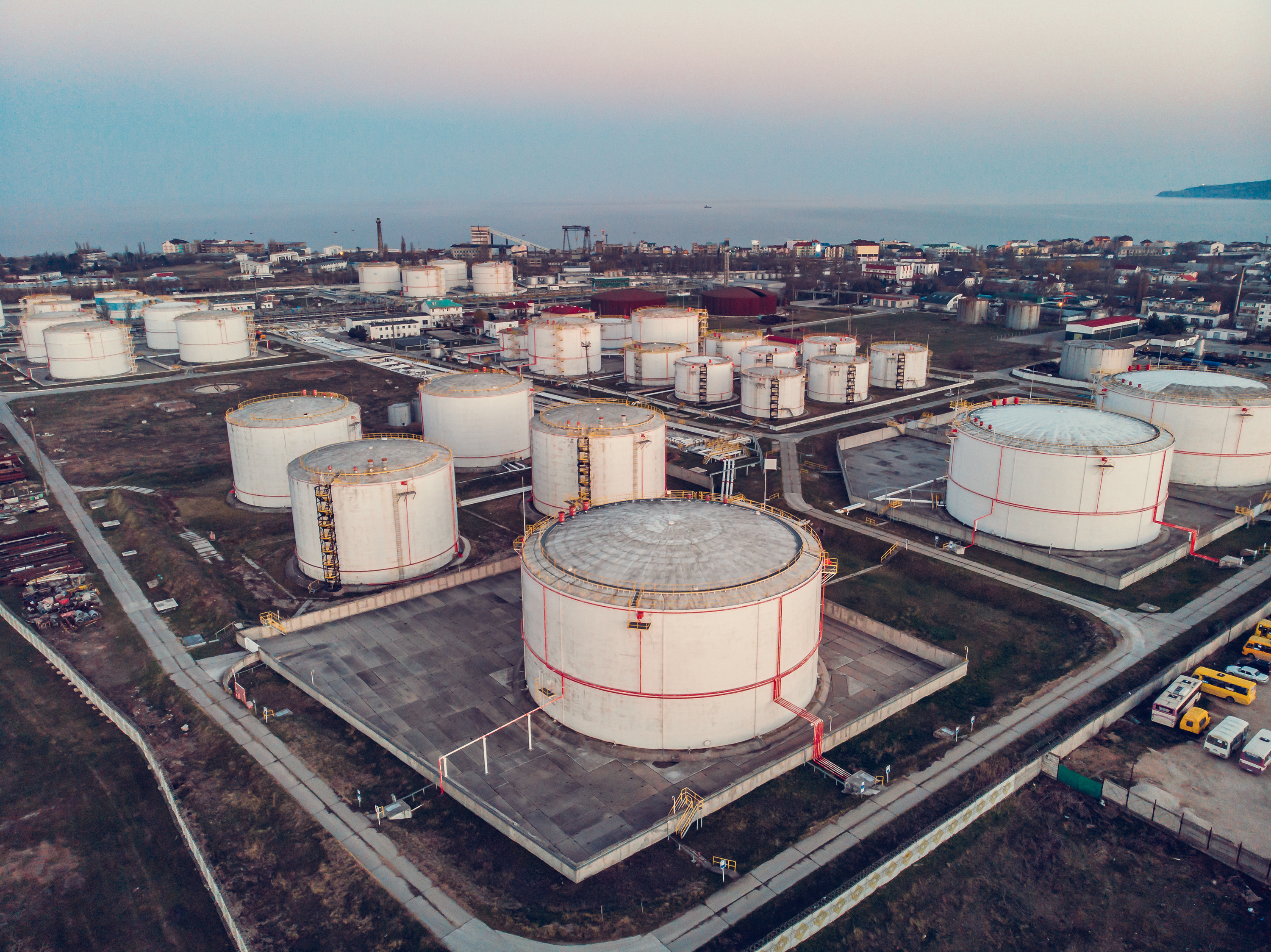 Aerial view of steel round Oil Storage Tanks or Reservoirs at sunset. Oil refinery industry, petroleum and petrochemical plant, drone shot.