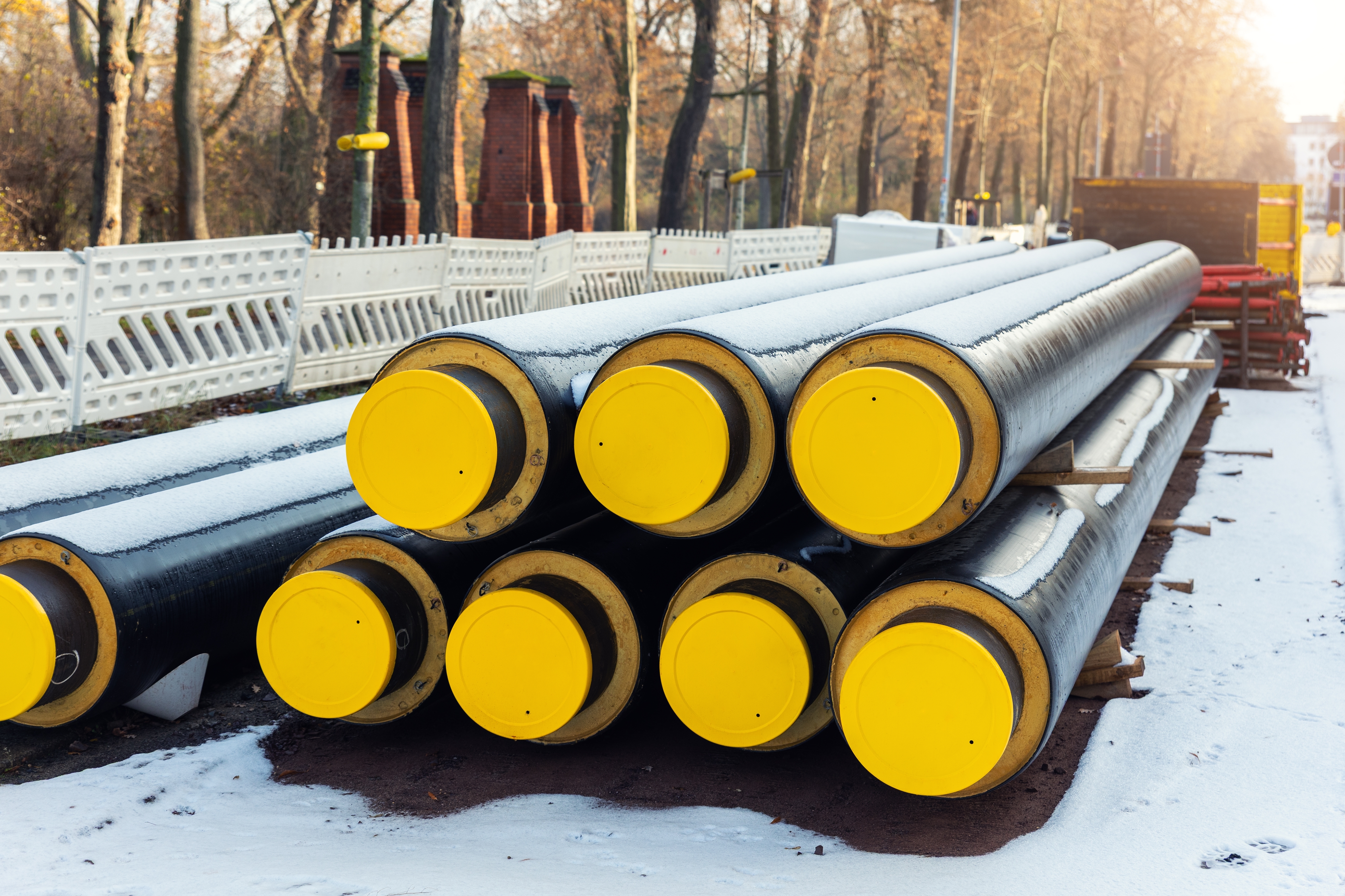 Photo showing insulated district heating pipes covered in snow and stacked on an urban construction site shutterstock 2717548235