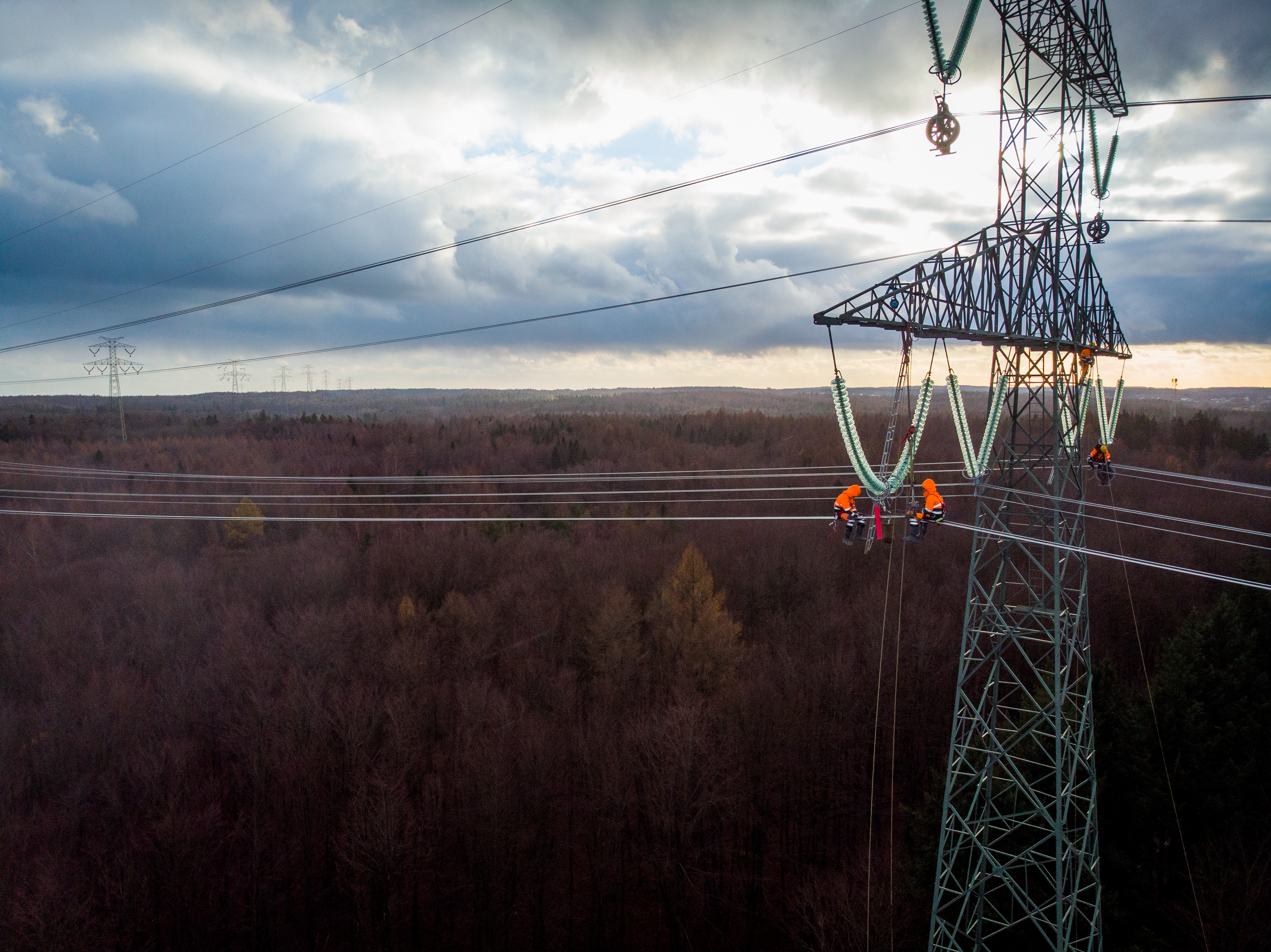 photo depicts and aerial view of electricians working on electric poles to install and repair power lines