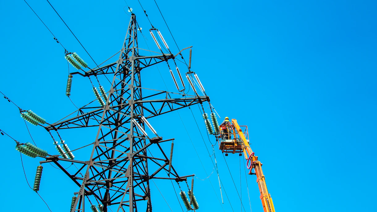 Portada de la construcción de la futura red de transmisión Línea eléctrica de alta tensión Torre de transmisión Trabajadores con grúa y cielo azul Shutterstock 2021650961