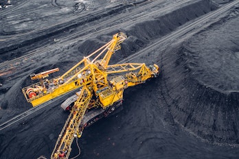 A photograph of a large coal mine and yellow heavy machinery