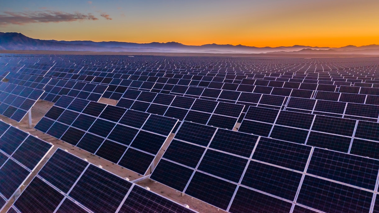 Photo depicts and aerial view of hundreds solar energy panels rows along the dry lands at Atacama Desert, Chile. Huge Photovoltaic PV Plant in the middle of the desert from an aerial drone point of view during sunset