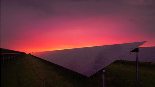 Photo depicts a black solar panel under red and grey clouds.