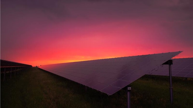 Photo of black solar panel under red and grey clouds.