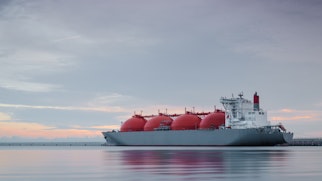 Photo shows a gas tanker ship in the water with a setting sun behind it