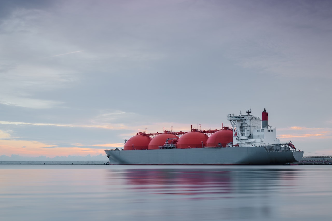 Photo shows a gas tanker ship in the water with a setting sun behind it