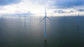 Photo shows a wind turbine in the forefront of the photo, with more turbines in the distance, all are in water