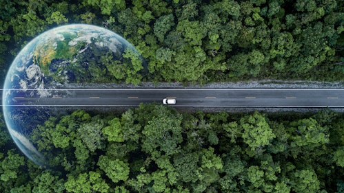 Photo shows a car driving alone on a highway road surrounded by green trees. A detailed earth photo is superimposed on the left