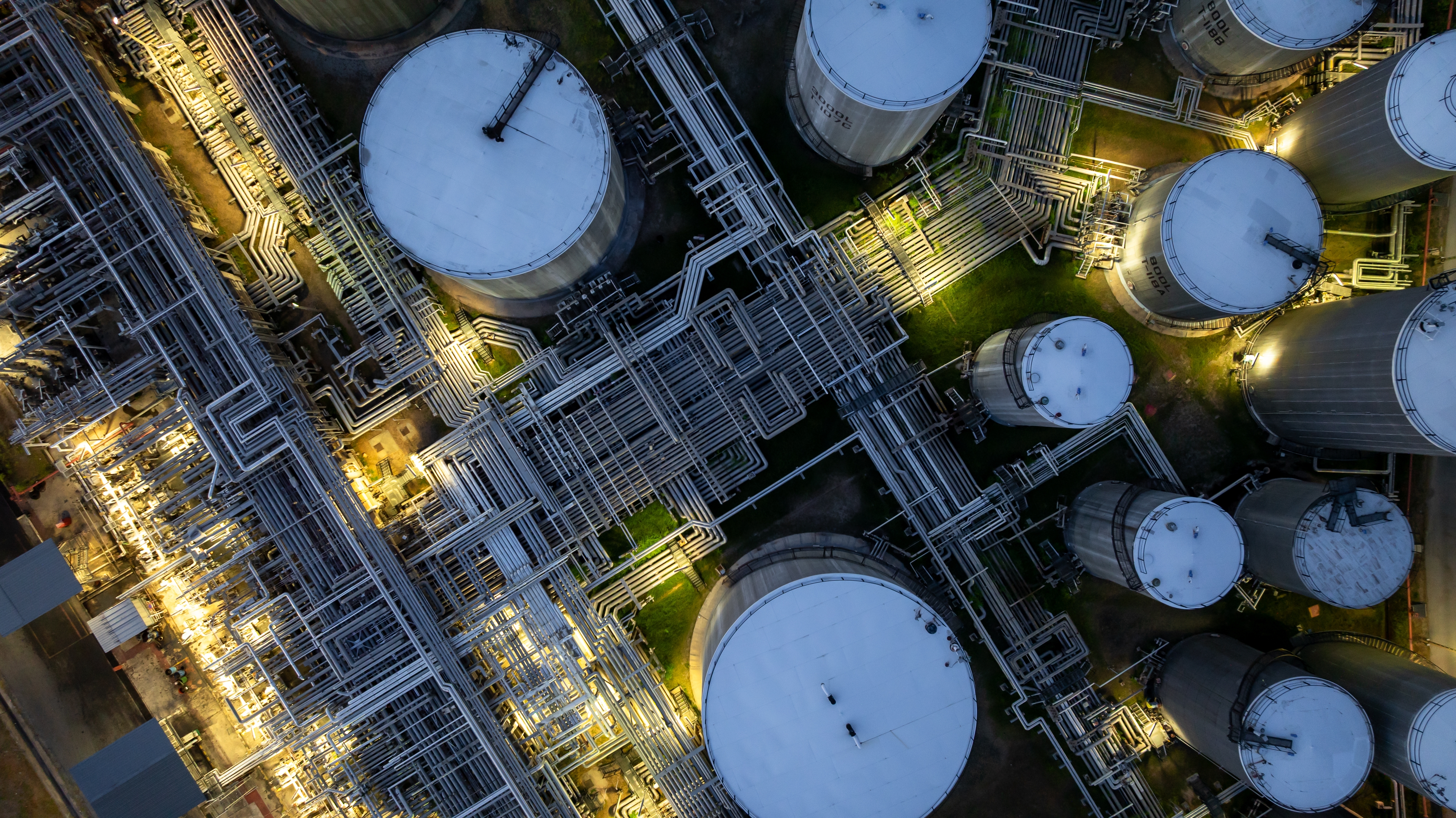 photo depicts Aerial view of oil storage tank and steel pipeline at night, oil storage tank, petroleum petrochemical refinery product, oil pipeline transportation system, steel pipeline to the oil refinery industry.