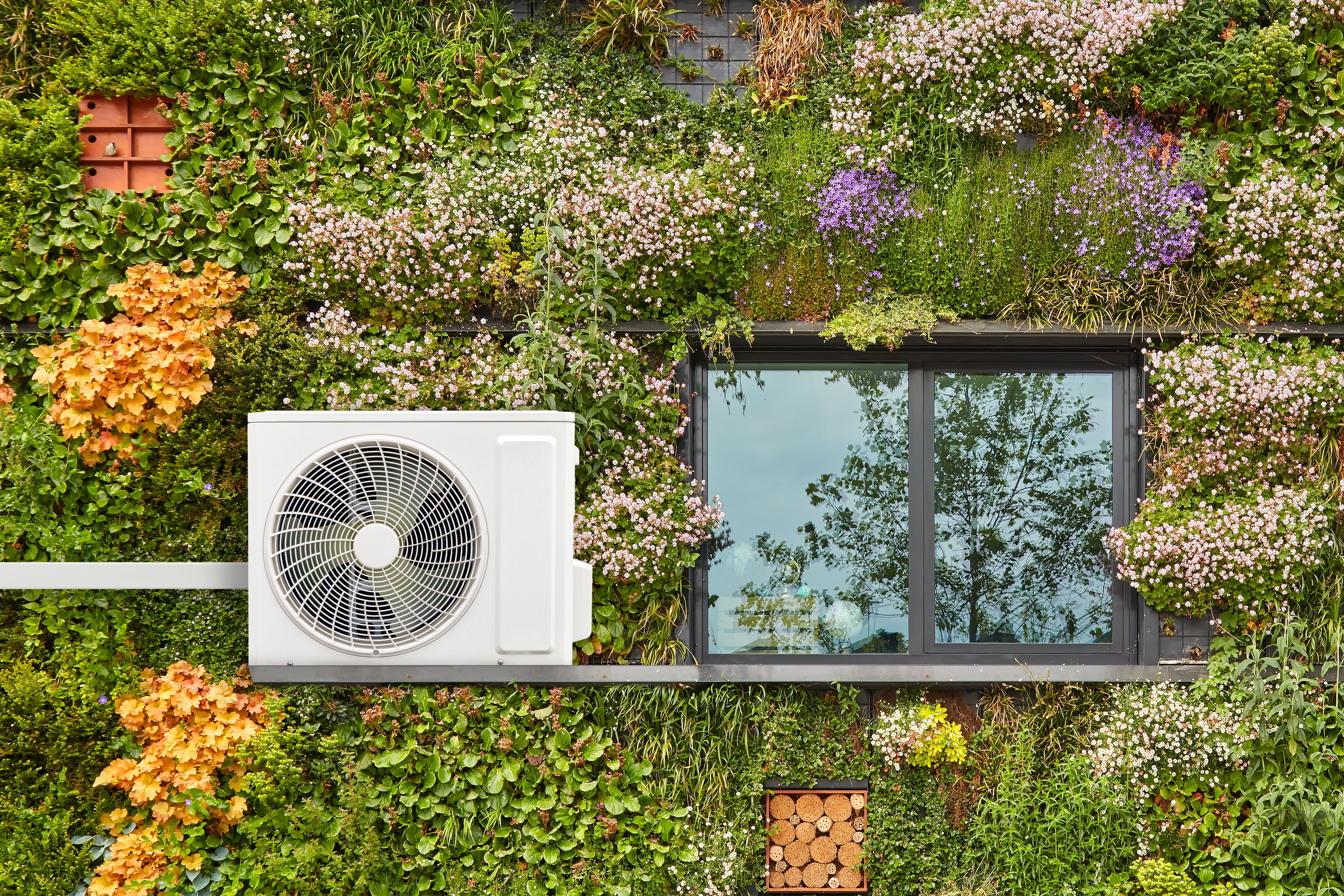 Air-source heat pump on a green, sustainable building covered with vertically hanging flowering plants