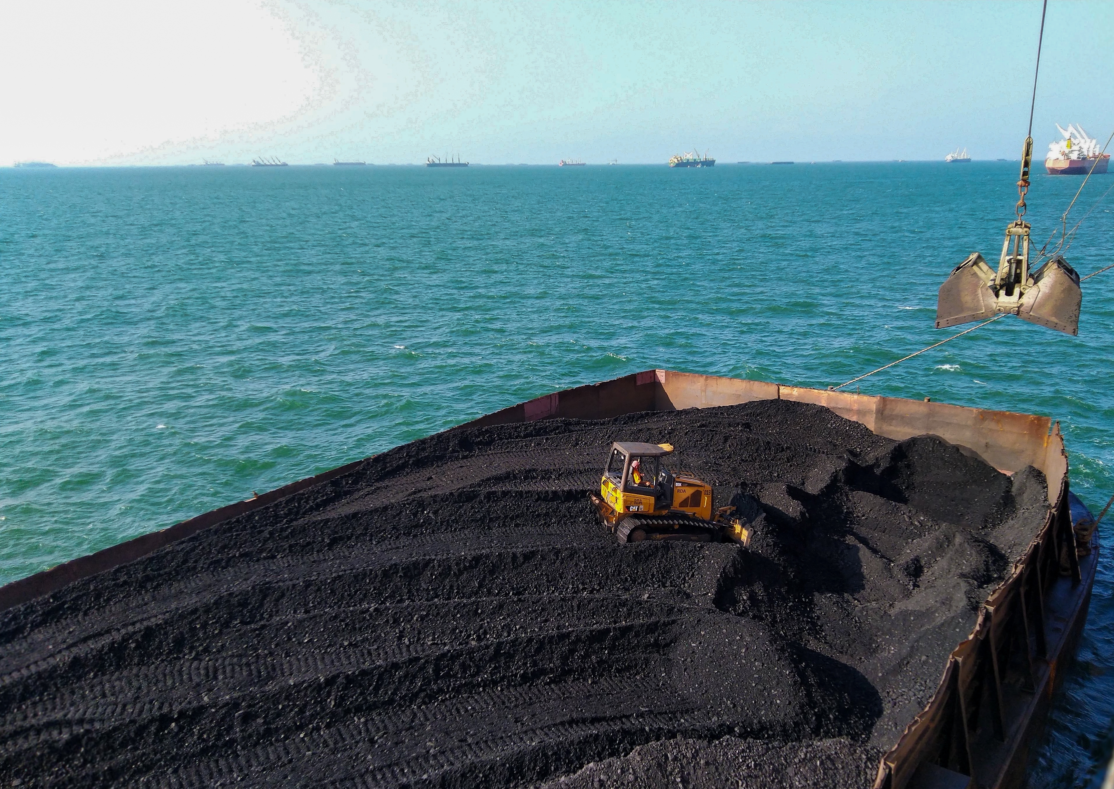Photo depicts a bulldozer helping the crane operator load coal from a barge onto a ship_Shutterstock 2511809669