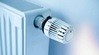 Photo depicts a White panel radiator with a modern thermostat on the wall in an apartment - selective focus