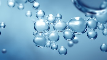 The photo depicts a studio shot of fizzing bubbles of transparent blue gas levitating in macro view with defocused plume blur.