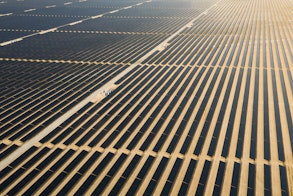Photo depicts an Aerial view of a landscape with photovoltaic solar panel farm producing sustainable renewable energy in a desert power plant.