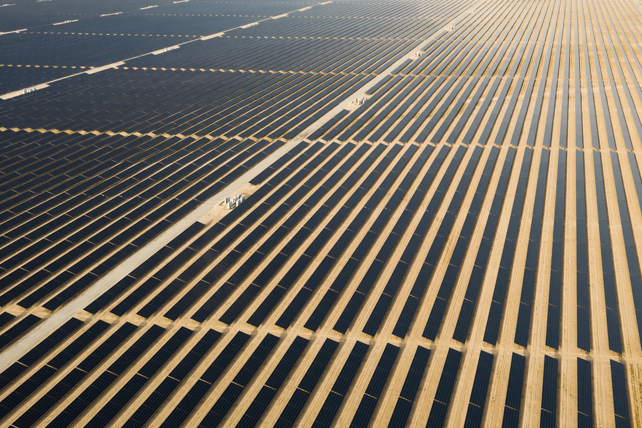 Photo depicts an Aerial view of a landscape with photovoltaic solar panel farm producing sustainable renewable energy in a desert power plant.