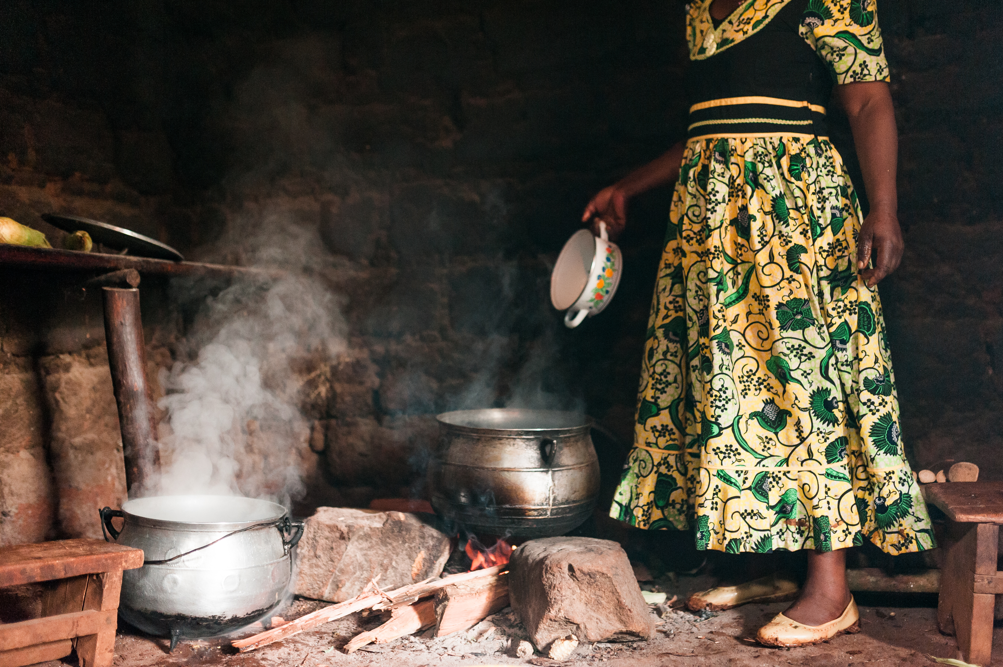 Photo depicts An elderly African woman cooks traditional fufu in a small village kitchen with smoke